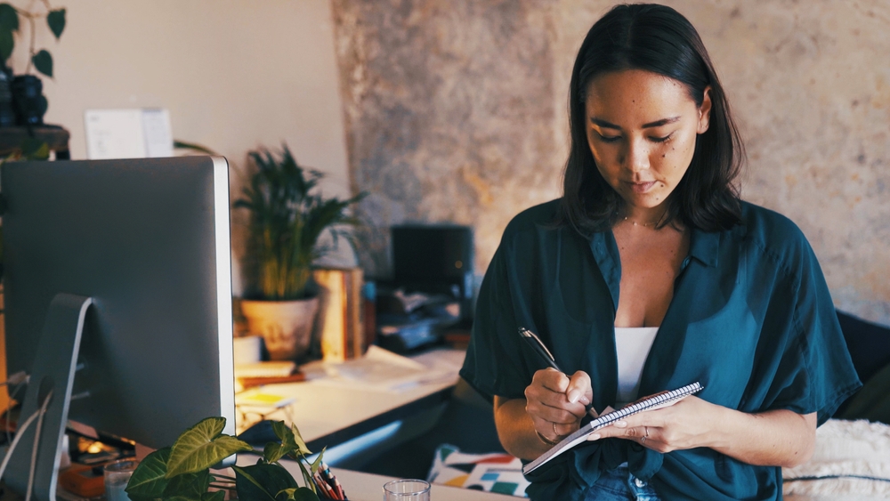 Remote work, woman and writing in notebook in home office for appointment, schedule or reminder