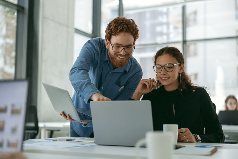Two diverse business colleagues discuss biz issue while use laptop in office background